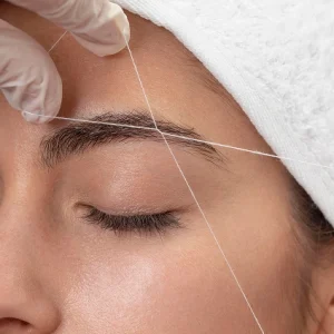 mujer haciendo la depilación de las cejas con hilo a una clienta